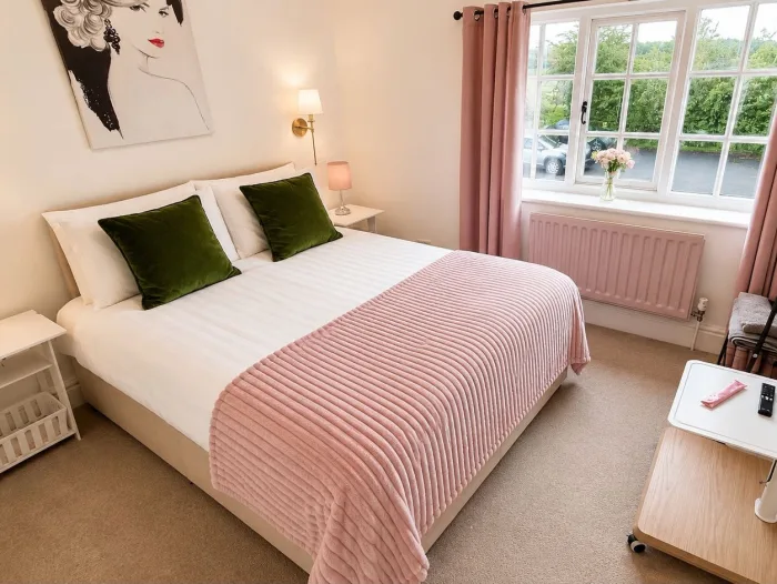 A made-up double bed with green cushions, a lamp on either side and a window onto the trees